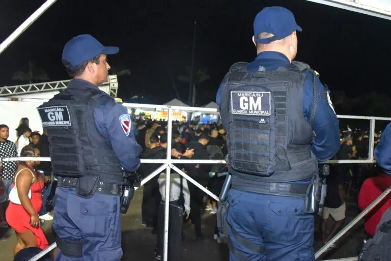 Agentes de segurança durante evento em Maricá, com viaturas e público ao fundo, reforçando a segurança.