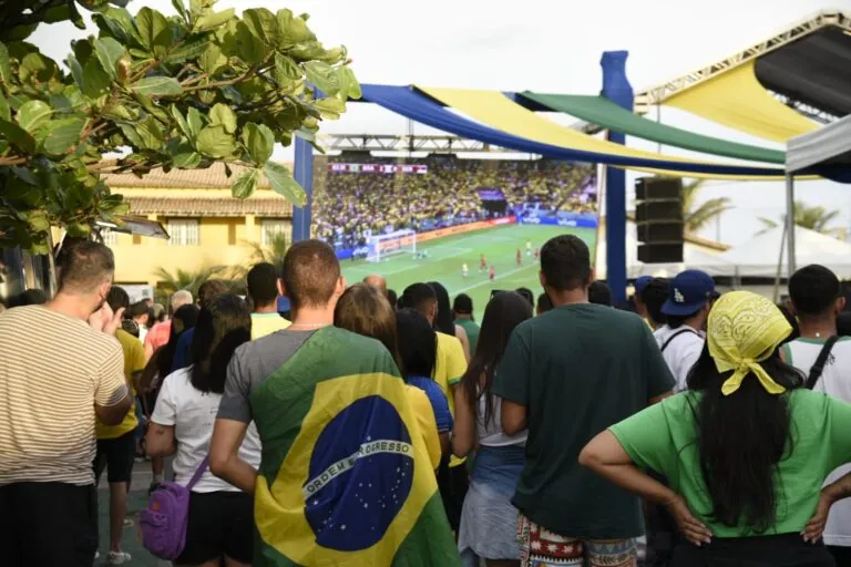 Telão exibindo jogo de futebol em praça pública com público celebrando em Maricá durante a Copa do Mundo 2026.