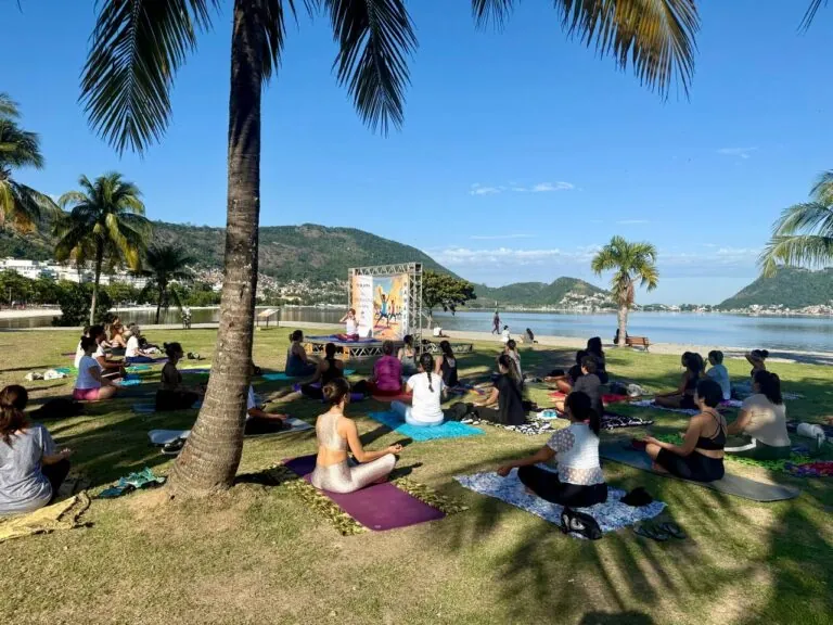 Pessoas praticando yoga ao ar livre em um parque, com a cidade de Niterói ao fundo, representando a aula gratuita.