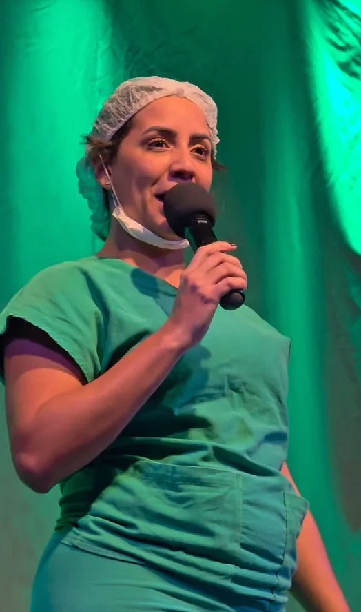 Humorista Camila Cardoso no palco fazendo stand-up comedy para plateia em São Gonçalo.