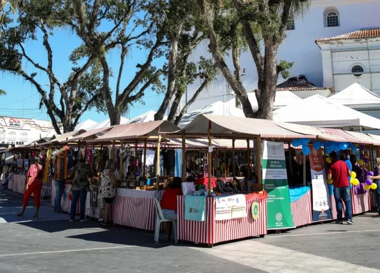 Pessoas em feira ao ar livre na Praça Orlando de Barros Pimentel, em Maricá, celebrando a Moeda Mumbuca.