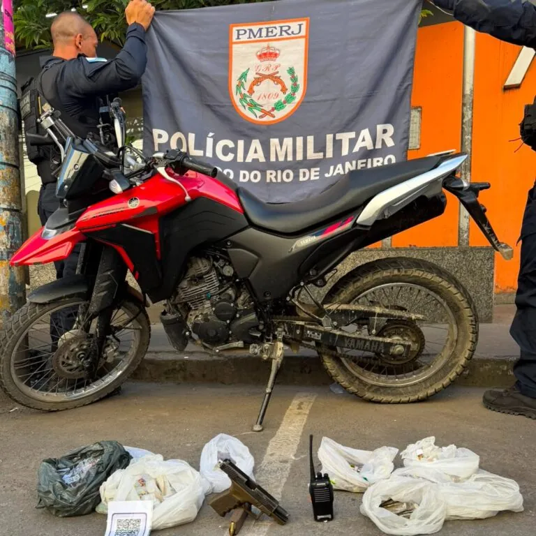 Policiais militares em operação no Jardim Catarina, São Gonçalo, com materiais apreendidos: pistola, rádio, motocicleta e drogas.