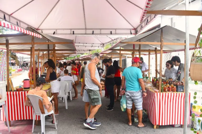 Pessoas comprando produtos frescos e artesanato em barracas da Feira da Agricultura Familiar em Maricá.