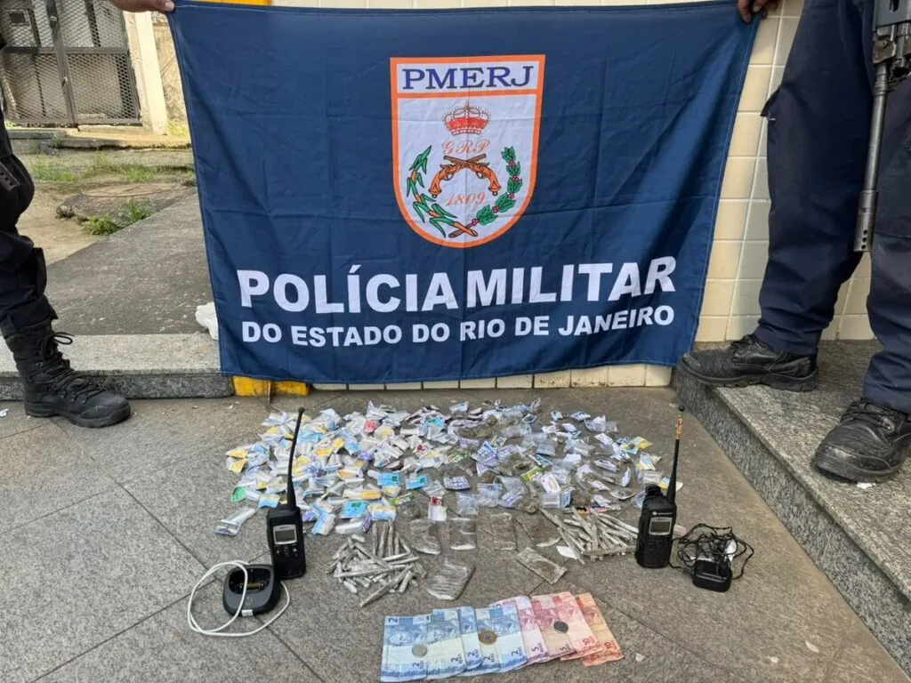 Policiais militares exibem drogas apreendidas, como maconha, cocaína e crack, junto com rádios e dinheiro em Niterói.