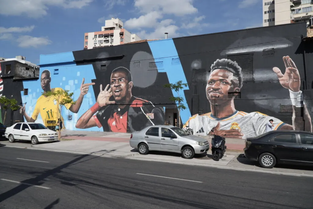 Alunos observam mural de arte urbana em São Gonçalo durante o Circuito Pedagógico Cidade Ilustrada, aprendendo sobre a história local.