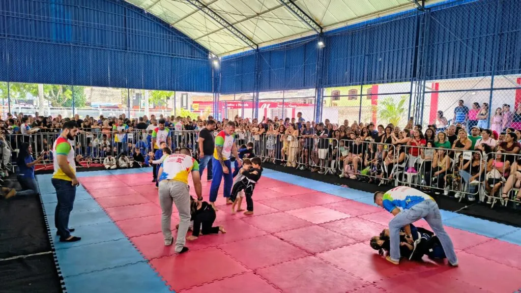 Atletas de jiu-jítsu em tatame durante festival em Maricá, com público ao fundo.